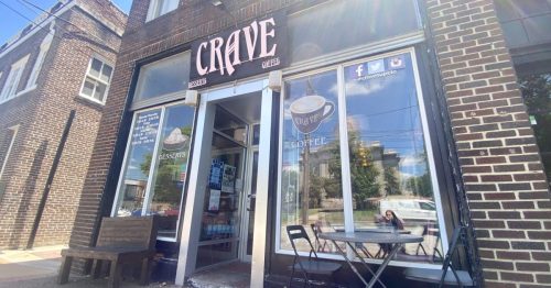 Exterior of Crave Coffee shop featuring a sign, large windows, and a small outdoor seating area.