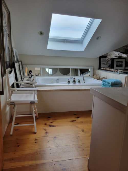 Bright bathroom with a skylight, featuring a bathtub, wooden floor, and a white chair.