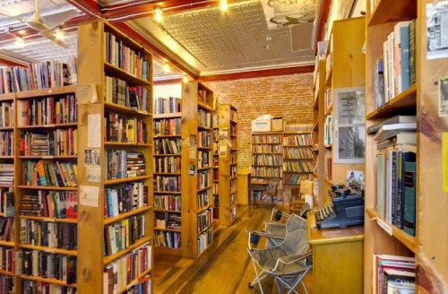 A cozy bookstore with wooden shelves filled with books, a typewriter, and chairs for reading. Warm, inviting atmosphere.