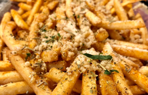 A close-up of golden French fries topped with herbs and grated cheese.