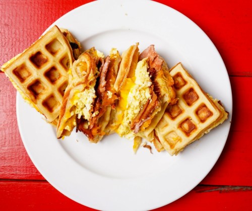 A plate of waffles filled with scrambled eggs and ham, served on a vibrant red table.