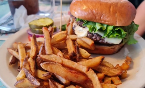 A juicy burger with lettuce and cheese, served with a side of crispy fries and pickles on a plate.