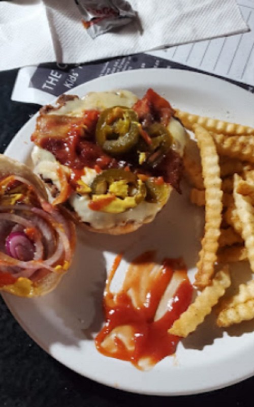 A burger topped with cheese, jalapeños, and onions, served with crinkle-cut fries and ketchup on a plate.
