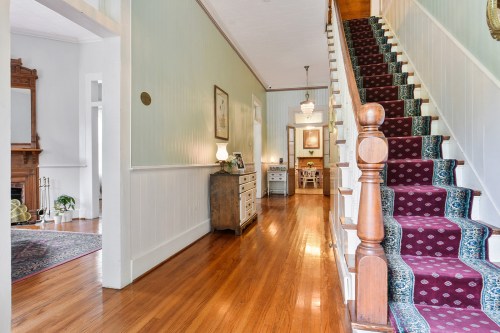 A bright hallway with wooden floors, a staircase, and a view of a dining area in a charming home.