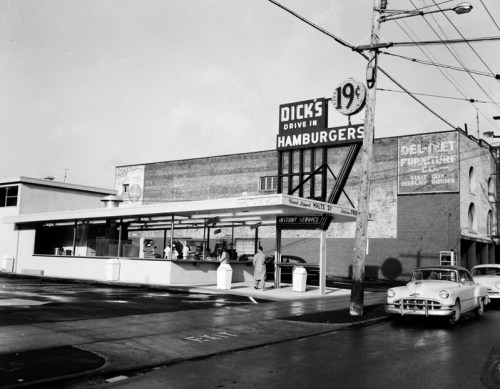 Black and white photo of Dick's Drive-In, featuring a retro sign and a classic car parked nearby.
