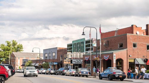A bustling street scene with shops, a theater, and parked cars under a cloudy sky.