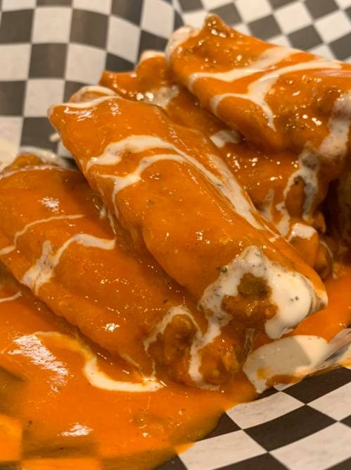 A close-up of rolled tortillas smothered in orange sauce and drizzled with white sauce, served in a checkered basket.
