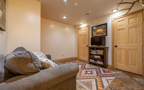 Cozy interior space featuring a gray couch, a patterned rug, a TV, and wooden doors. Warm lighting enhances the ambiance.