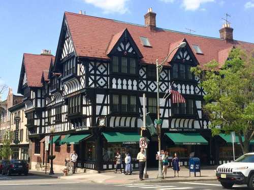 A historic building with a black and white facade, featuring a steep roof and green awnings, on a busy street corner.