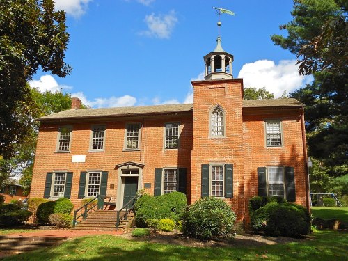 Historic brick building with a cupola, surrounded by greenery and under a blue sky with scattered clouds.