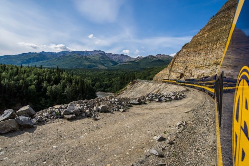 A scenic view of a winding train track along a mountainous landscape with lush greenery and rocky terrain.