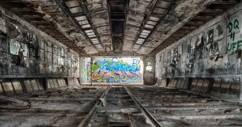 Abandoned interior of a building with graffiti on the wall and debris scattered on the floor.