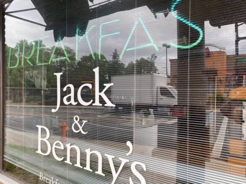 A storefront window displaying the words "Breakfast" and "Jack & Benny's" with a reflection of the outside.