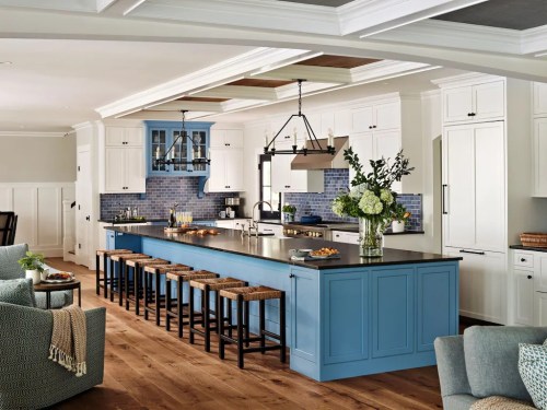 Modern kitchen with blue island, white cabinets, and wooden floors, featuring bar stools and floral arrangements.