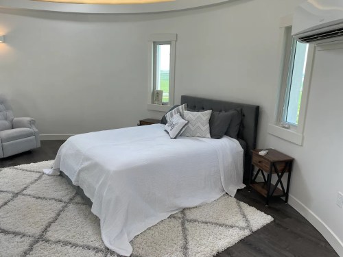 A modern bedroom featuring a gray bed, white bedding, two nightstands, and large windows with a view.