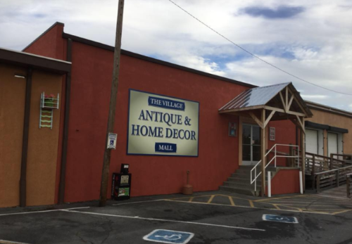 Exterior of a building with a sign that reads "The Village Antique & Home Decor Mall," featuring a staircase and awning.