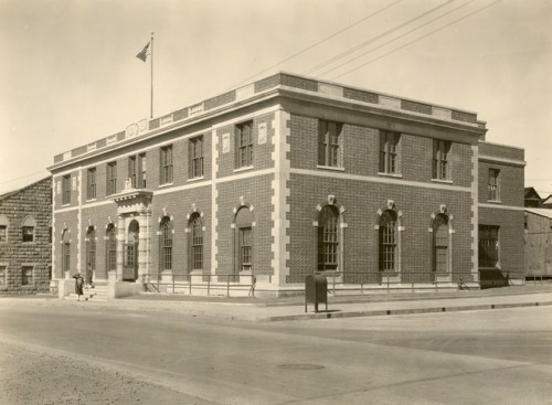 Historic brick building with arched windows, an American flag, and a mailbox outside, set on a quiet street.