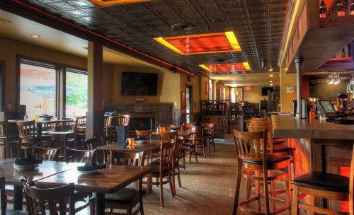 Interior of a restaurant featuring wooden tables, chairs, and a bar area with warm lighting and a cozy atmosphere.