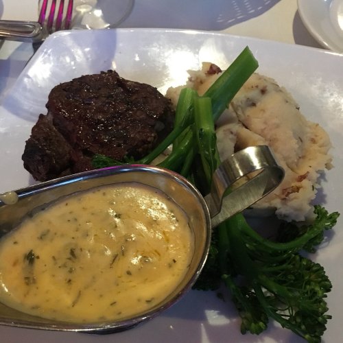 A plate featuring a grilled steak, mashed potatoes, broccolini, and a small gravy boat with sauce.