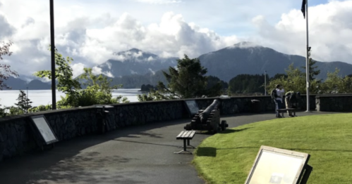 A scenic view of mountains and water, featuring a stone wall, cannons, and informational signs in a park setting.
