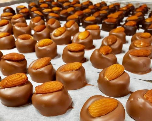 A close-up of rows of chocolate-covered candies topped with almonds, arranged neatly on parchment paper.