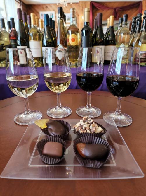 A selection of wine glasses filled with white and red wine, alongside a plate of assorted chocolates on a table.