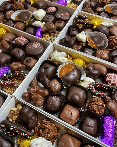 A close-up of assorted chocolates in boxes, featuring various shapes, colors, and toppings.
