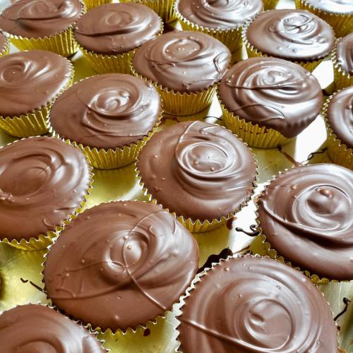 A close-up of freshly made cupcakes topped with smooth chocolate frosting in gold liners, arranged on a tray.