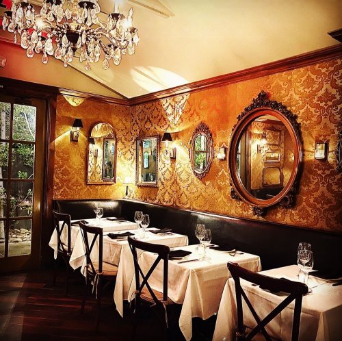 Elegant restaurant interior with chandeliers, ornate mirrors, and white tablecloths, creating a warm, inviting atmosphere.