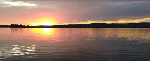 A serene sunset over a calm lake, with vibrant orange and purple hues reflecting on the water's surface.