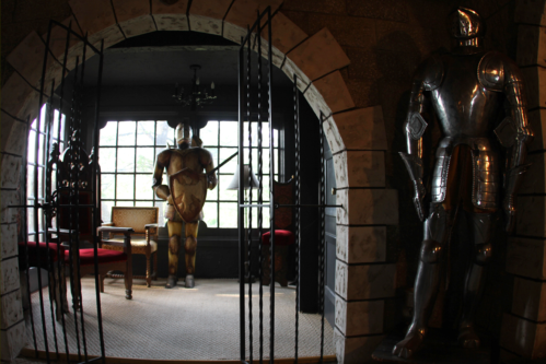 A medieval room featuring two suits of armor, a chair, and large windows, creating a historic atmosphere.
