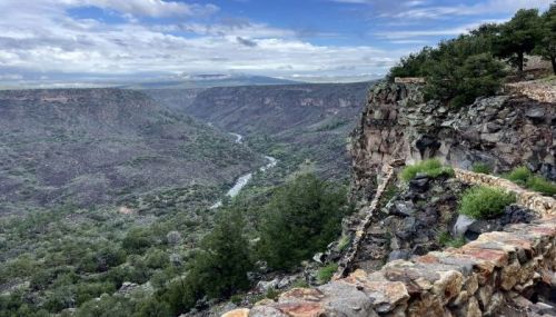 A scenic view of a river winding through a canyon, surrounded by rocky cliffs and lush greenery under a cloudy sky.
