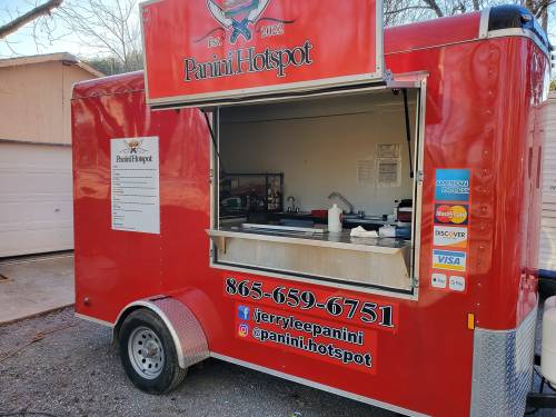 Red food truck with "Panini Hotspot" signage, featuring a service window and contact information.