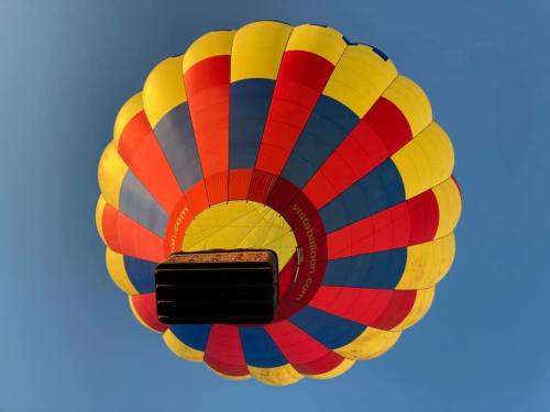 A colorful hot air balloon with red, yellow, and blue panels against a clear blue sky.