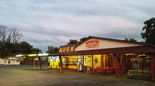A retro diner with bright yellow and orange signage, outdoor seating, and a cloudy evening sky.