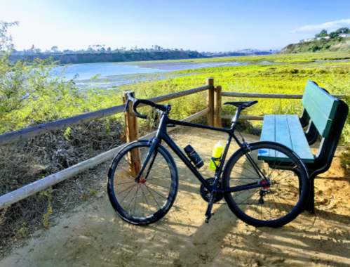 A black bicycle parked next to a green bench by a serene waterway surrounded by lush vegetation.