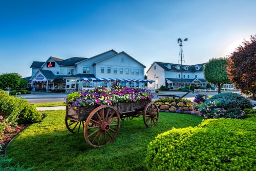 A charming building with flower-filled wagon in front, surrounded by lush greenery and a windmill in the background.