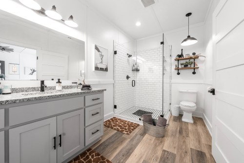 Modern bathroom featuring a glass shower, gray vanity, and wooden accents on the floor and shelves.