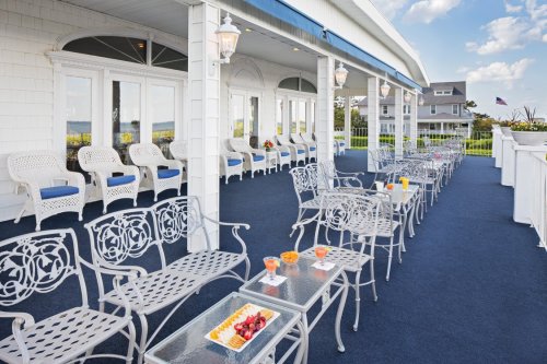 A spacious outdoor patio with white metal chairs, tables, and fruit platters, overlooking a scenic view.