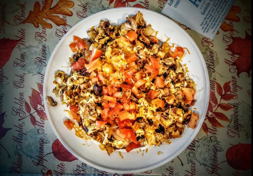 A plate of chopped chicken topped with tomatoes, cheese, and spices, served on a decorative tablecloth.