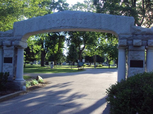 Archway reading "Brookside" at the entrance of a park, surrounded by trees and a paved pathway.