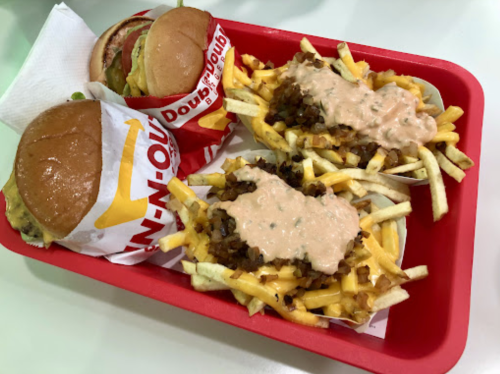 A red tray with two burgers and two servings of fries topped with sauce.
