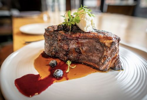 A beautifully plated steak topped with herbs and a dollop of cream, drizzled with berry sauce on a white plate.