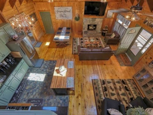 Cozy cabin interior with wooden floors, a living area, dining table, and a fireplace, featuring rustic decor.