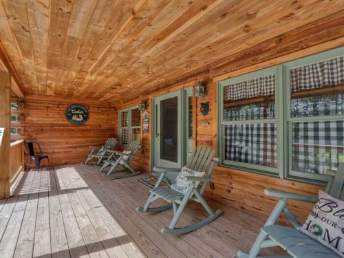 A cozy wooden porch with rocking chairs and checkered curtains, inviting relaxation in a rustic setting.