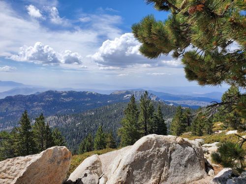 A scenic mountain view with lush green trees, rocky outcrops, and a blue sky dotted with clouds.