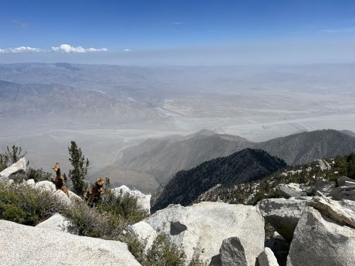 A panoramic view of a mountainous landscape with rocky terrain and a hazy valley below under a clear blue sky.