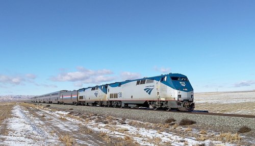 An Amtrak train travels along a snowy landscape under a clear blue sky.