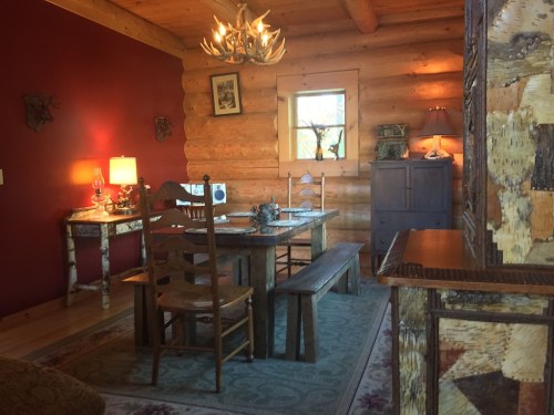 Cozy log cabin interior featuring a dining table, wooden chairs, and warm lighting against a rustic backdrop.