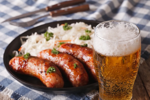 A plate of grilled sausages with sauerkraut and a glass of beer on a checkered tablecloth.